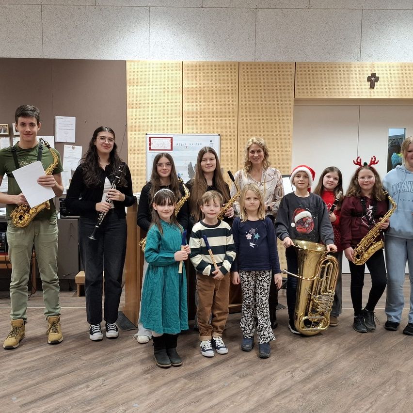 Eine Gruppe junger Musiker, darunter Kinder und Erwachsene, posiert für ein Foto in einem Raum und hält verschiedene Musikinstrumente in den Händen.