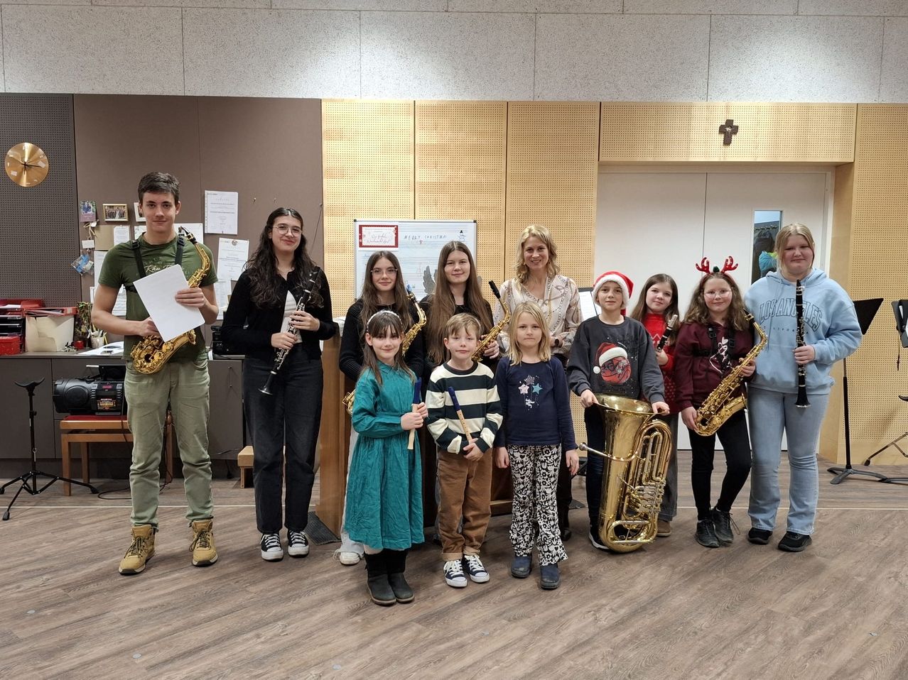 Eine Gruppe junger Musiker, darunter Kinder und Erwachsene, posiert für ein Foto in einem Raum und hält verschiedene Musikinstrumente in den Händen.