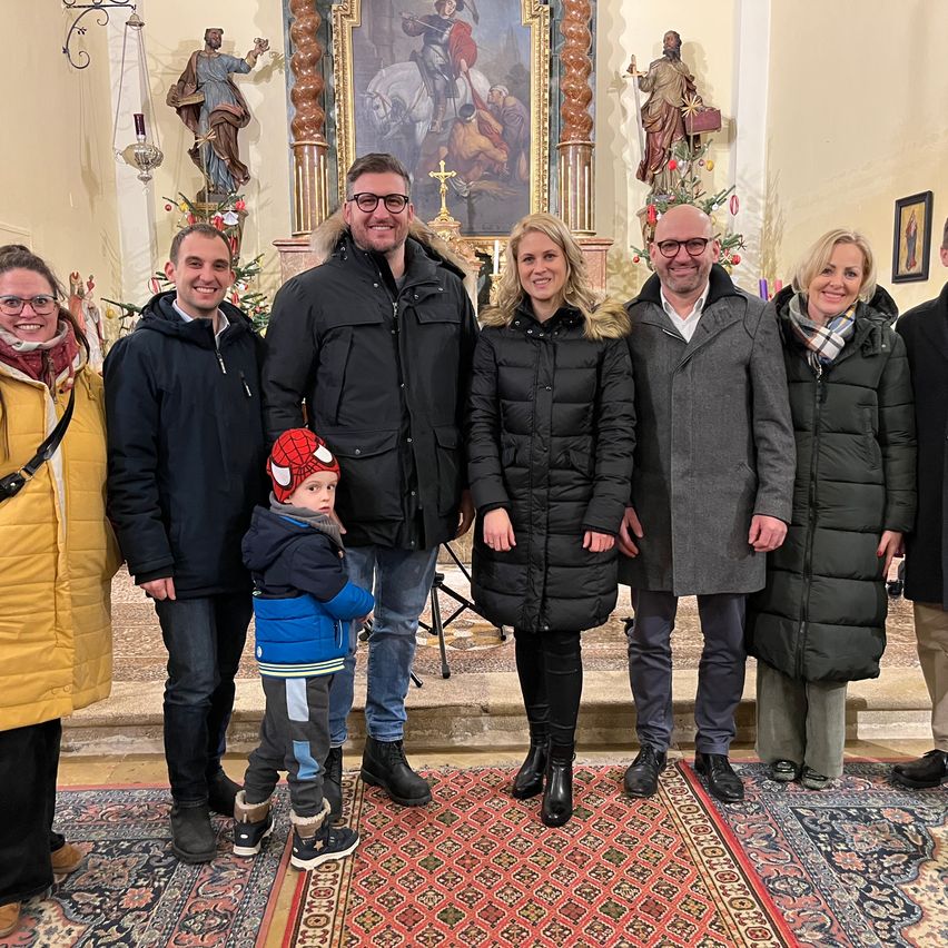 Eine Gruppe von Menschen, darunter ein Kind mit einer Spider-Man-Mütze, posiert für ein Foto in einer Kirche mit religiösen Statuen und einem Weihnachtsbaum im Hintergrund.