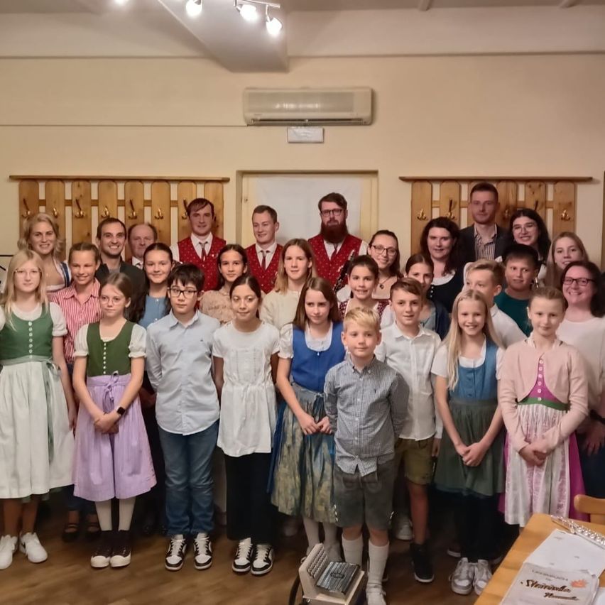 Eine Gruppe von Menschen in traditionellen Kostümen posiert für ein Foto in einem Raum mit Holzmöbeln und einer Klimaanlage.