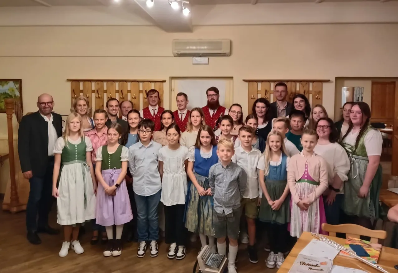 Eine Gruppe von Menschen in traditionellen Kostümen posiert für ein Foto in einem Raum mit Holzmöbeln und einer Klimaanlage.