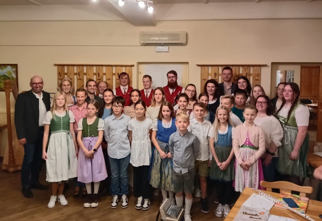 Eine Gruppe von Menschen in traditionellen Kostümen posiert für ein Foto in einem Raum mit Holzmöbeln und einer Klimaanlage.