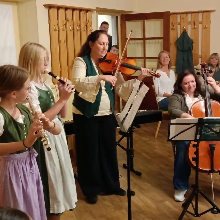 Eine Gruppe von Frauen übt gemeinsam Musik. Eine Frau spielt die Geige, eine andere die Flöte und eine dritte Frau spielt die Geige. Sie alle lächeln und scheinen die Musik zu genießen.