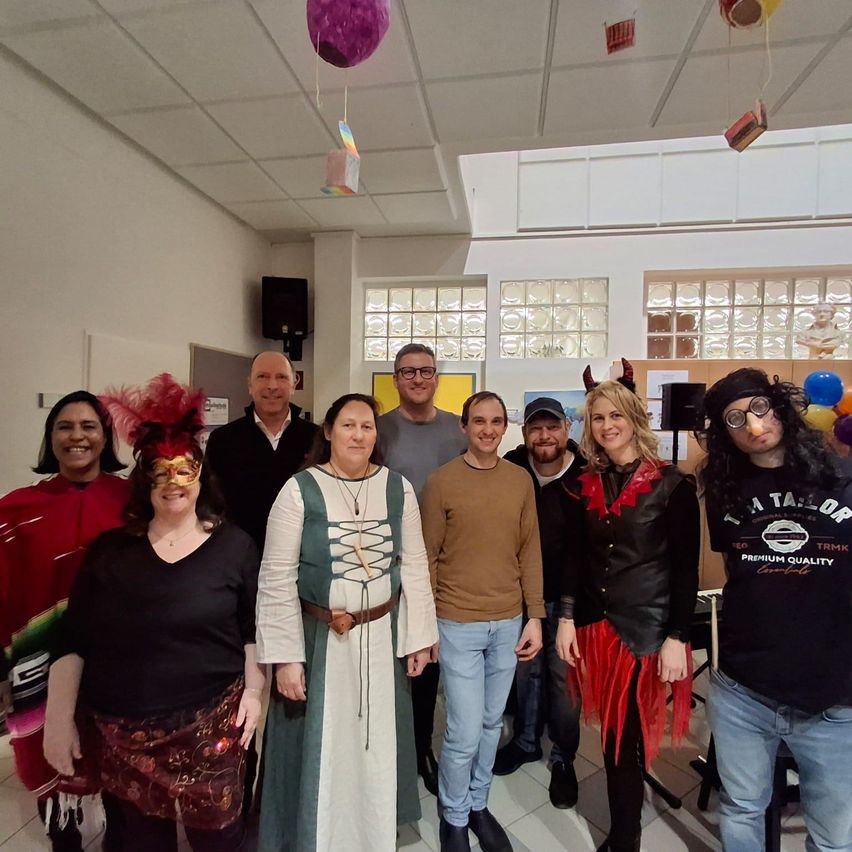 Eine Gruppe von Menschen in Kostümen und Masken posiert für ein Foto in einem Raum mit Luftballons und einer weißen Decke.