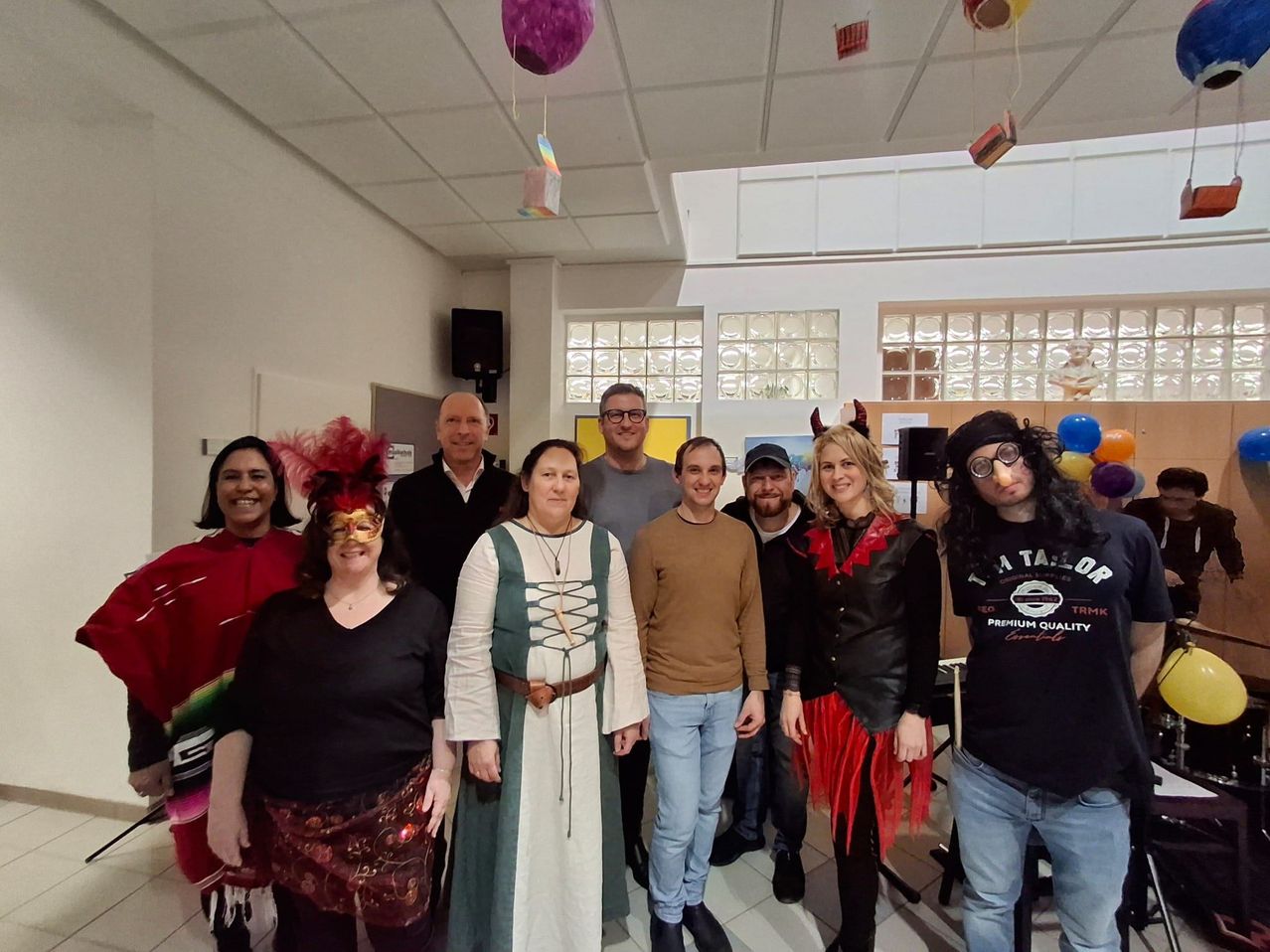 Eine Gruppe von Menschen in Kostümen und Masken posiert für ein Foto in einem Raum mit Luftballons und einer weißen Decke.