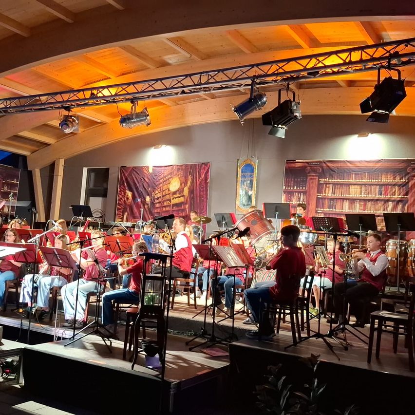 Eine Gruppe junger Musiker spielt auf der Bühne mit verschiedenen Instrumenten unter Bühnenlicht in einer Innenumgebung.