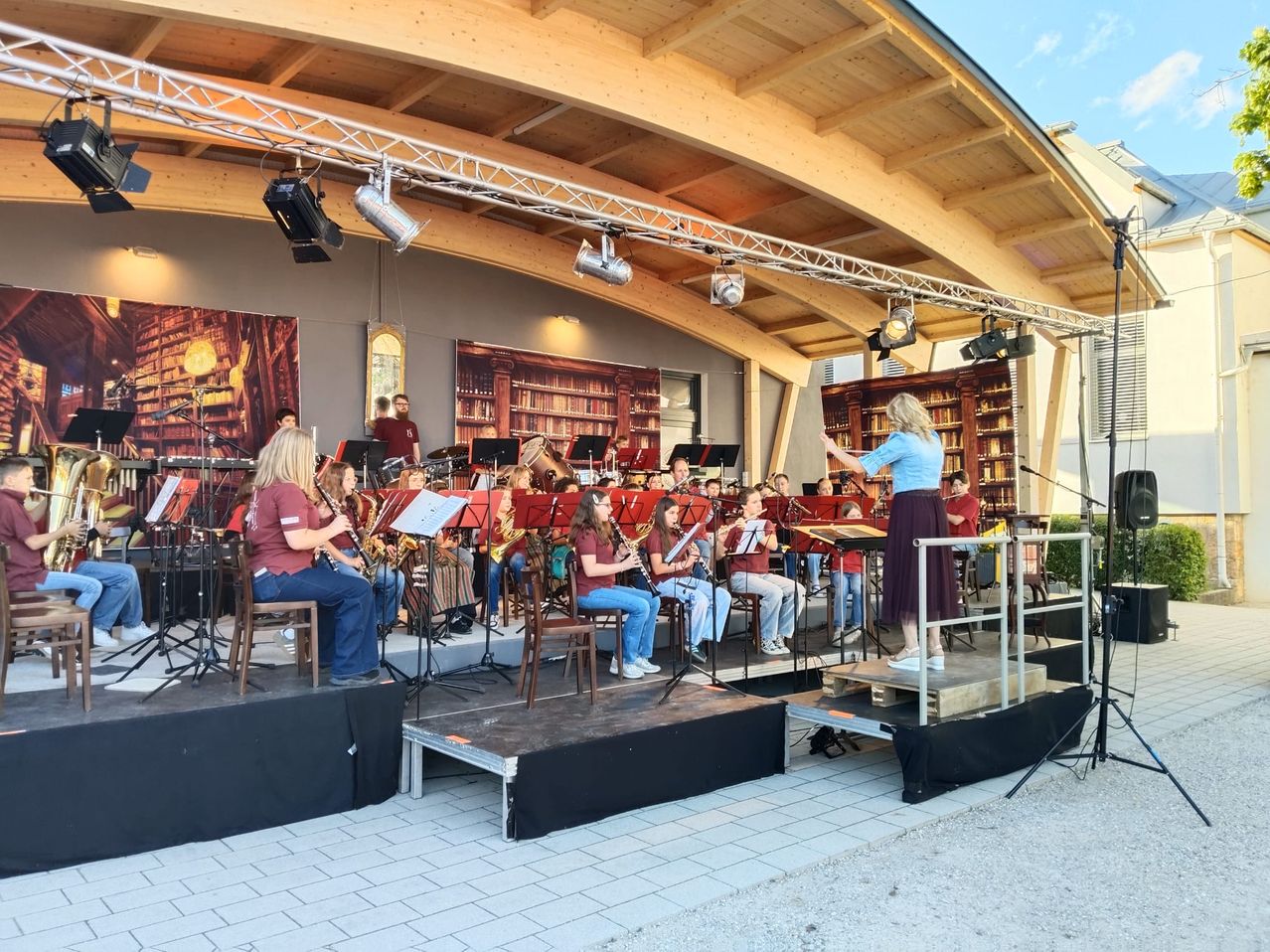 Eine Band spielt auf der Bühne mit einer Frau davor. Einige spielen Blasinstrumente. Es gibt Lichter und ein Mikrofon auf der Bühne.