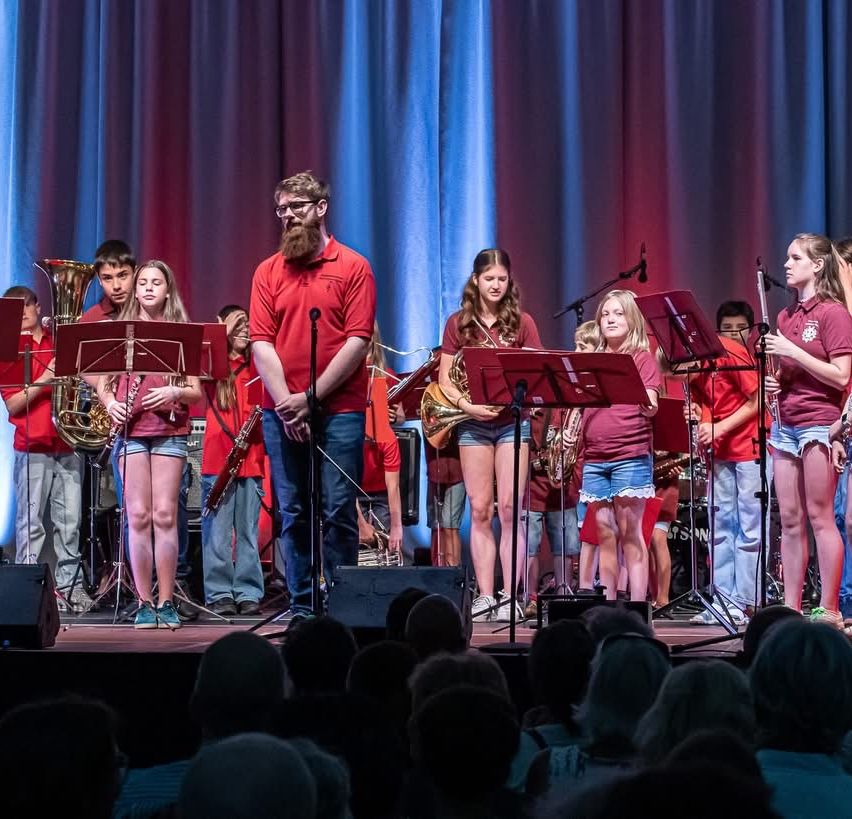 Eine Band steht mit Instrumenten wie Posaunen und Flöten auf der Bühne und tritt vor einem Publikum auf.