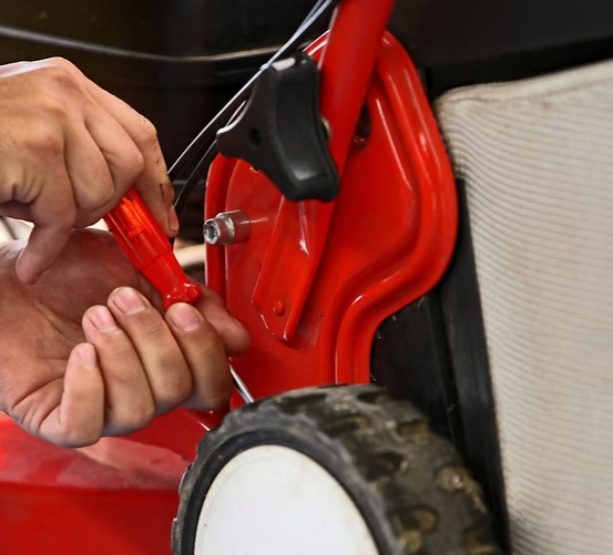 Eine Person benutzt einen roten Schraubendreher, um an einem roten Rasenmäher zu arbeiten und eine Schraube zu justieren.