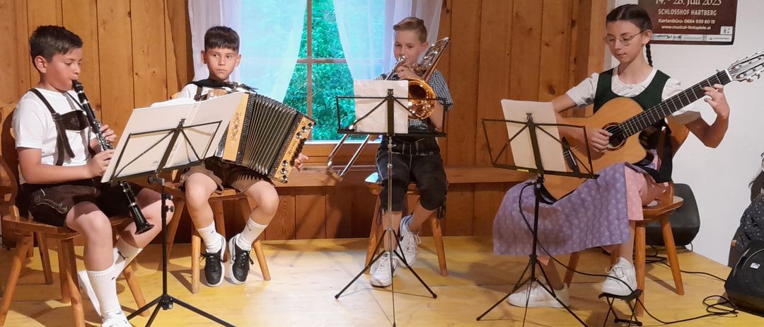 Zwei Jungen spielen Musikinstrumente in einem Raum. Einer spielt Akkordeon und der andere Posaune. Sie sitzen auf Stühlen mit Notenständern vor ihnen.