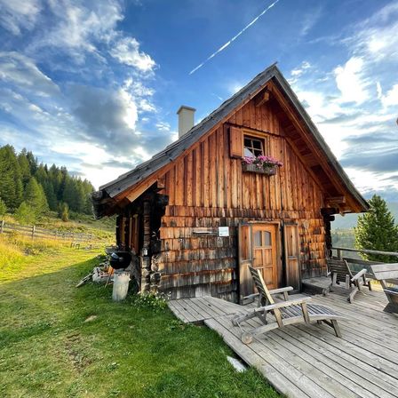 Ein Holzchalet mit Balkon und Blumen am Fenster. Ein Holzstuhl auf der Veranda.