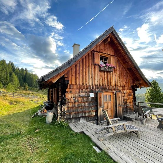 Ein Holzchalet mit Balkon und Blumen am Fenster. Ein Holzstuhl auf der Veranda.