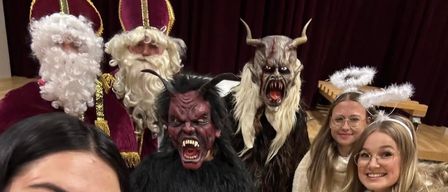 Eine Gruppe von Menschen in Kostümen, zwei Frauen mit Brille, eine in einer weißen Jacke, eine in einem schwarzen und weißen Kostüm, eine in einem roten und weißen Kostüm und eine in einem pelzigen weißen Kostüm.
