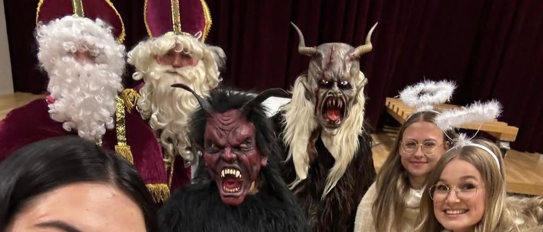 Eine Gruppe von Menschen in Kostümen, zwei Frauen mit Brille, eine in einer weißen Jacke, eine in einem schwarzen und weißen Kostüm, eine in einem roten und weißen Kostüm und eine in einem pelzigen weißen Kostüm.
