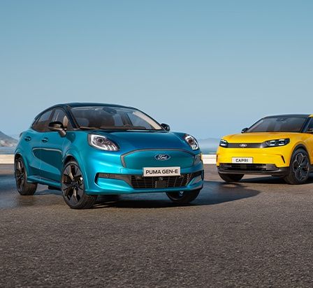 Drei Ford Autos, ein blauer Puma Gen-E, ein gelber Capri und ein grauer Explorer, geparkt in einer malerischen Außenumgebung.