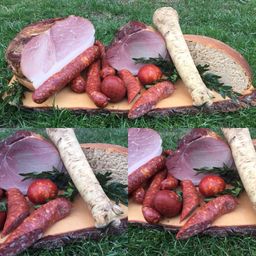 Ein Holzbrett zeigt verschiedene Fleisch- und Gemüsesorten, darunter Schinken, Würste und Kräuter, auf einer Rasenfläche.