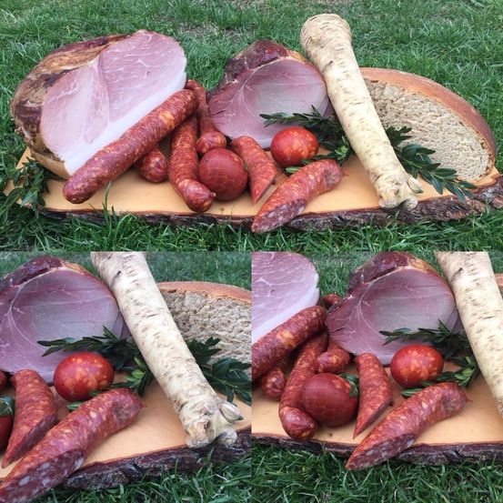 Ein Holzbrett zeigt verschiedene Fleisch- und Gemüsesorten, darunter Schinken, Würste und Kräuter, auf einer Rasenfläche.
