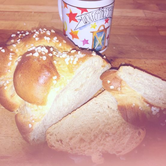 Geschnittenes Brot mit einer geflochtenen Oberseite, mit Zucker bestreut, liegt auf einer Holzoberfläche mit einer dekorativen Tasse.