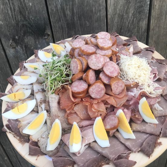 Ein Teller mit verschiedenen Fleischsorten, Würsten, Eiern und Käse. Die Fleischsorten und Eier sind kreisförmig angeordnet.