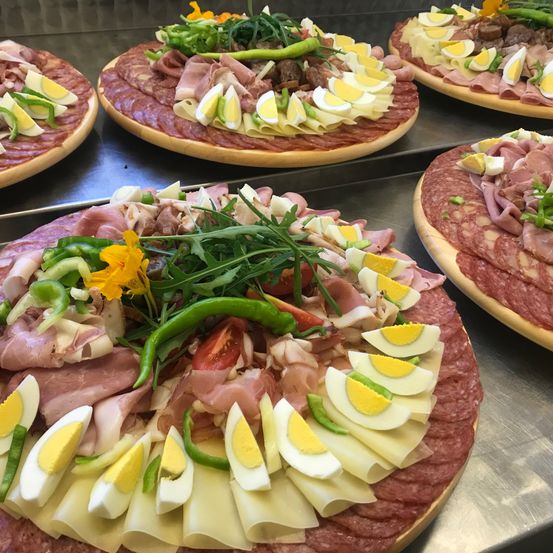 Eine Nahaufnahme mehrerer Charcuterie-Bretter mit Scheiben von Wurst, Käse, Eiern und Gemüse, die auf einem Metalltablett angeordnet sind.