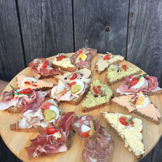 Ein Holzteller zeigt verschiedene belegte Brote mit Fleisch, Eiern und Gemüse. Jedes Sandwich hat einzigartige Toppings wie Tomaten, Käse und Sprossen.