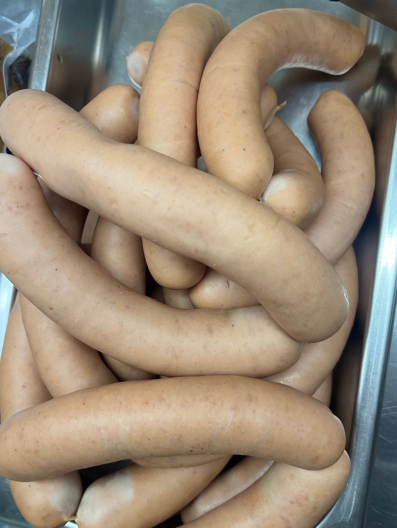 Eine Nahaufnahme von Würsten in einem Edelstahlbehälter. Die Würste haben verschiedene Größen und Formen, einige sind gewickelt und andere gerade.