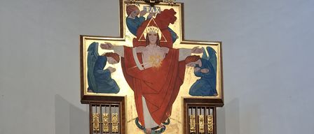 Ein Altar ist mit einer Kerze auf einem Tisch aufgebaut. Ein goldener Kelch ist auf einem Tuch platziert. Der Altar hat einen Kerzenhalter mit drei Kerzen. Ein Gemälde von Jesus Christus ist auf dem Altar ausgestellt. Topfpflanzen sind auf beiden Seiten des Altars platziert.