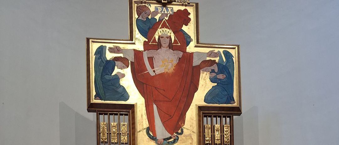 Ein Altar ist mit einer Kerze auf einem Tisch aufgebaut. Ein goldener Kelch ist auf einem Tuch platziert. Der Altar hat einen Kerzenhalter mit drei Kerzen. Ein Gemälde von Jesus Christus ist auf dem Altar ausgestellt. Topfpflanzen sind auf beiden Seiten des Altars platziert.