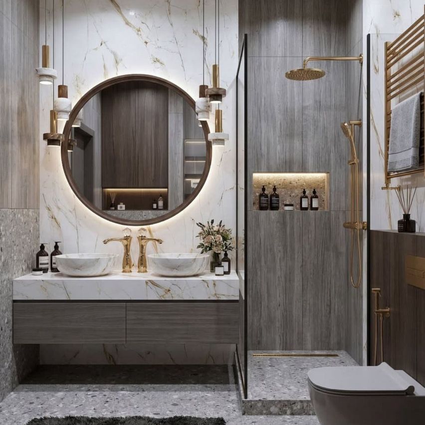 Ein elegantes Badezimmer mit einem runden Spiegel, goldenen Armaturen und Marmoroberflächen. Eine Glasdusche mit goldener Duschkopf befindet sich neben dem Waschbecken.