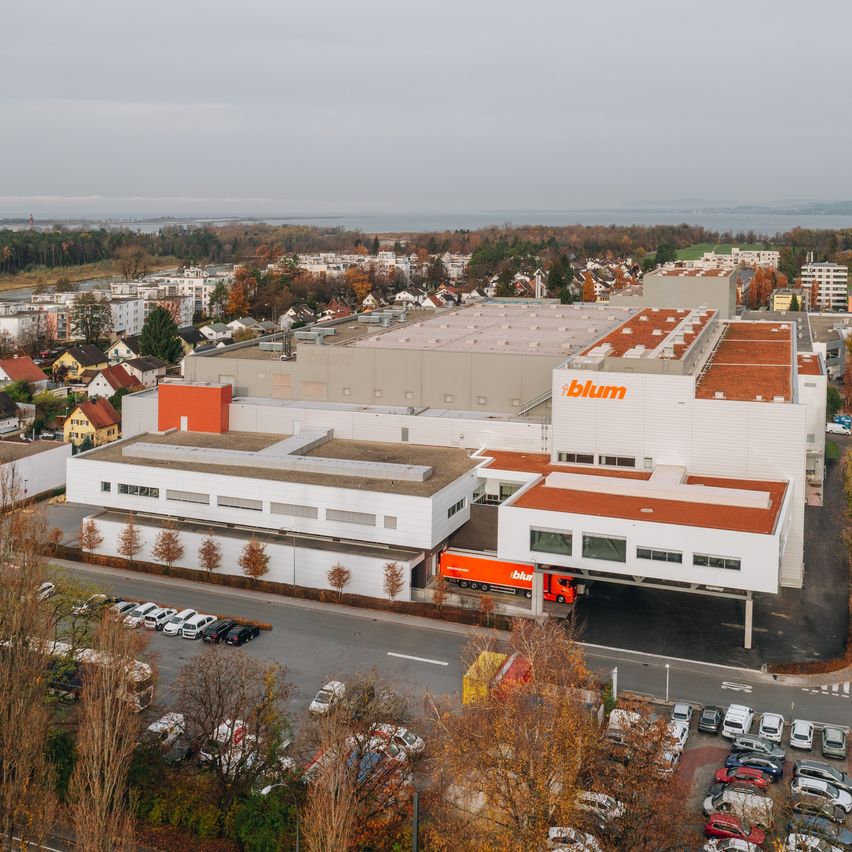 Ein Blick von oben auf eine Blum-Anlage mit einem großen weißen Gebäude und einem roten Blum-Logo. Verschiedene Autos sind um die Anlage herum geparkt.