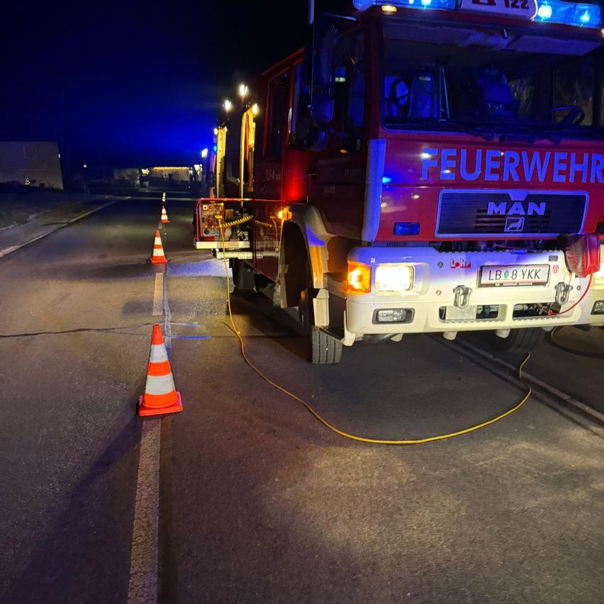 Ein Feuerwehrauto mit eingeschalteten Lichtern steht am Straßenrand, umgeben von Verkehrskegeln.