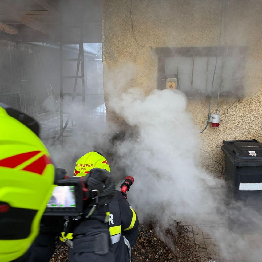 Firefighters are spraying water on a building with smoke coming out of it. A person is filming the scene.