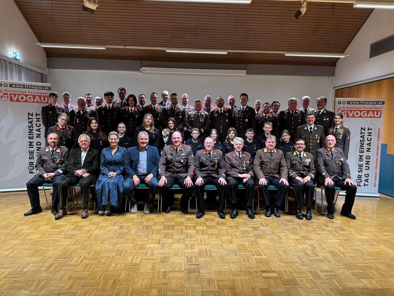 Eine große Gruppe von Militärangehörigen, sowohl Männer als auch Frauen, sitzen in Reihen auf grünen Stühlen in einem Raum. Sie tragen alle Uniform.