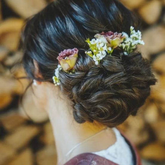Eine Frau mit schwarzem Haar in einem eleganten Hochsteckfrisur, geschmückt mit frischen Blumen, von hinten gesehen.