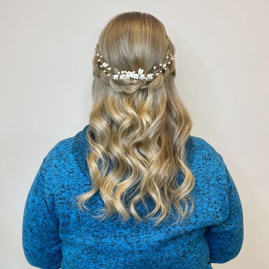 Eine Frau mit langen blonden Haaren trägt einen blauen Pullover und ein weißes Blumenhaaraccessoire.