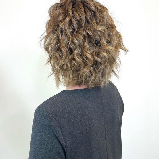 Die Rückseite einer Person mit kurzen, lockigen, blonden Haaren und einem grauen T-Shirt.