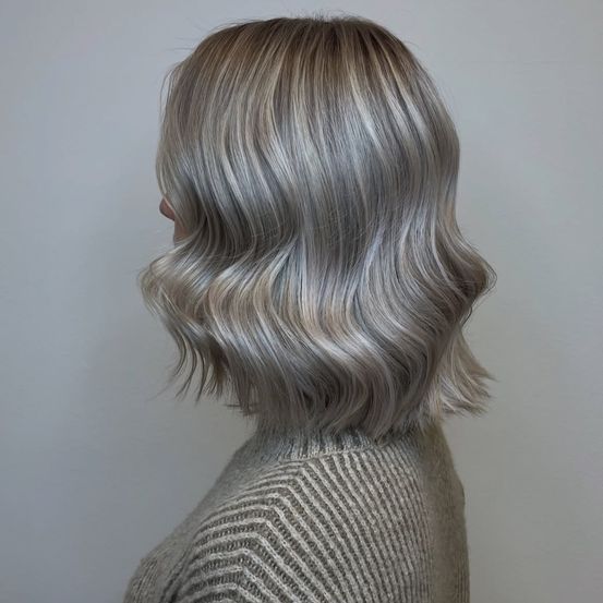 Eine Frau mit silberblonden, welligen Haaren, Rückansicht, trägt einen hellgrauen Pullover.