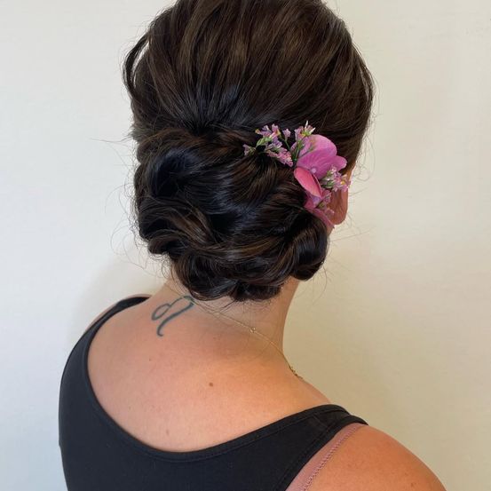 Eine Frau mit einer Blume im Haar trägt ein schwarzes ärmelloses Oberteil und hat eine Tätowierung auf der Schulter.