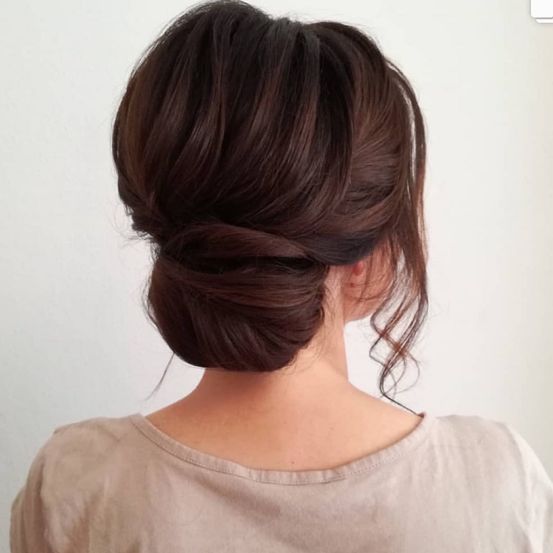 Die rückseitige Ansicht einer Frau zeigt ihr Haar in einem Dutt mit braunem Farbton. Sie trägt ein helles Oberteil.