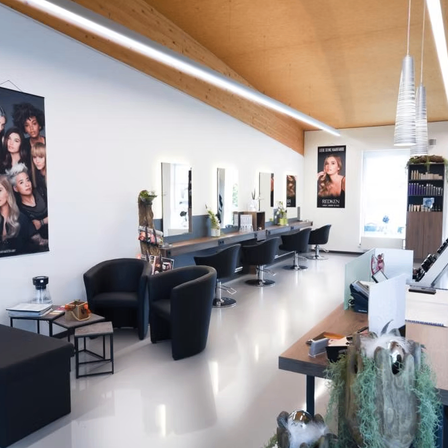 Ein Salon mit weißen Wänden und einer Holzdecke, ausgestattet mit Stühlen, Spiegeln, einem Schreibtisch und einem Plakat.