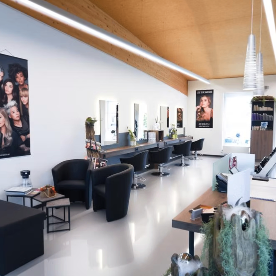 Ein Salon mit weißen Wänden und einer Holzdecke, ausgestattet mit Stühlen, Spiegeln, einem Schreibtisch und einem Plakat.