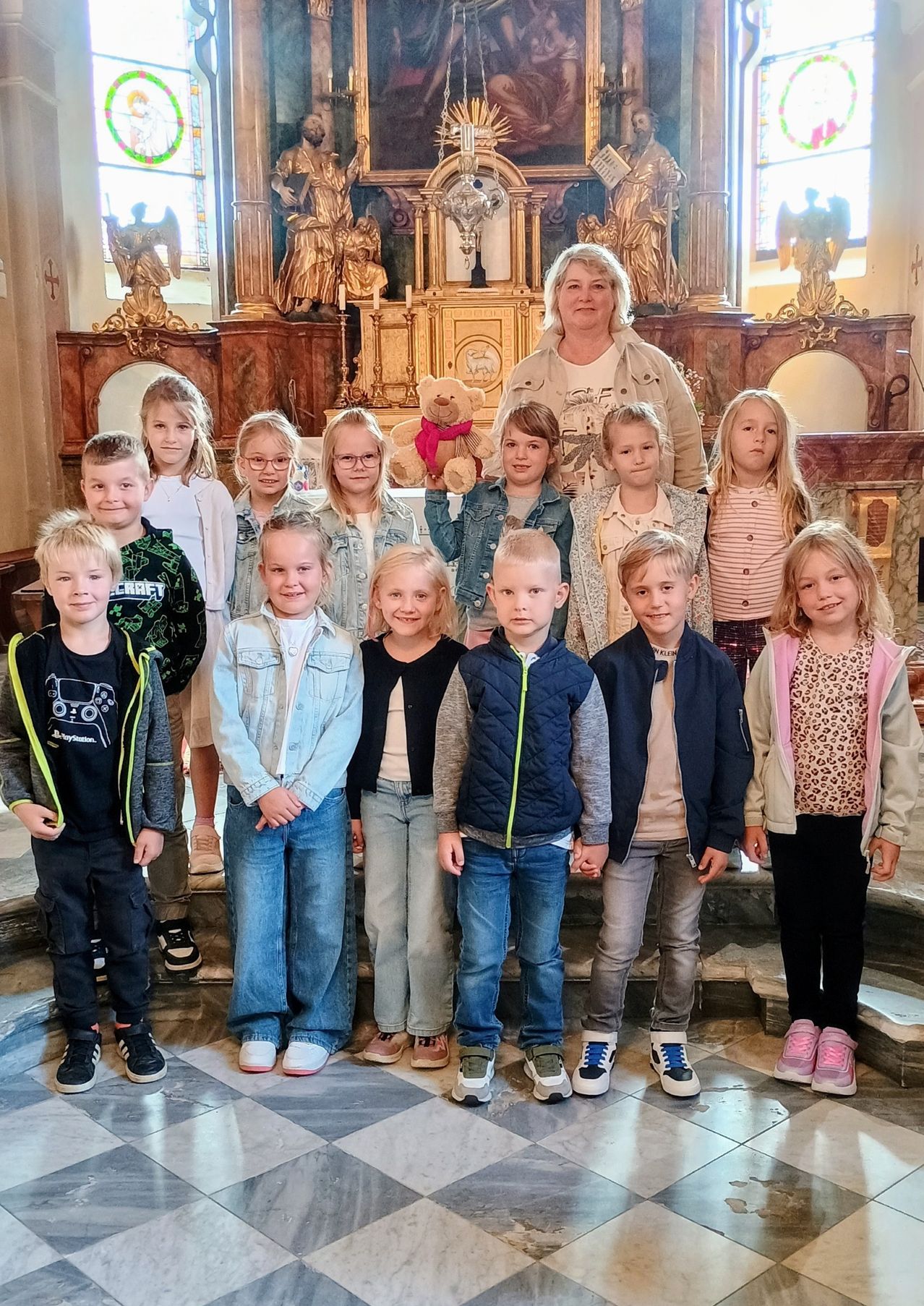 Eine Gruppe von Kindern und einer erwachsenen Frau posiert für ein Foto in einer Kirche mit Statuen und einem Altar im Hintergrund.
