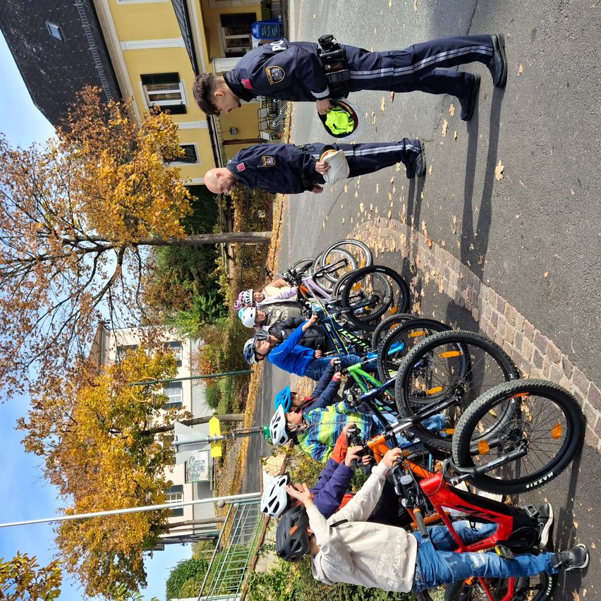 Polizeibeamte helfen Kindern, ihre Helme anzupassen und überprüfen ihre Fahrräder an einem sonnigen Tag.