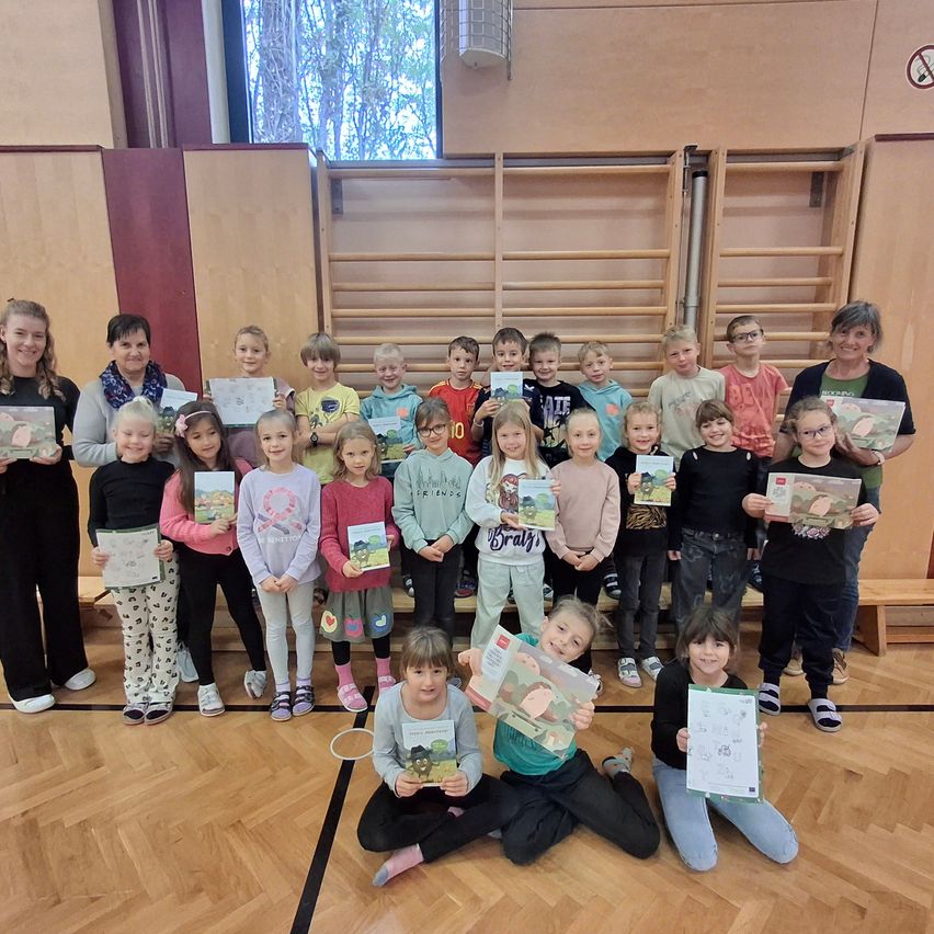 Eine Gruppe von Kindern in einer Turnhalle mit Erwachsenen, die Urkunden halten. Sie alle lächeln und schauen in die Kamera.
