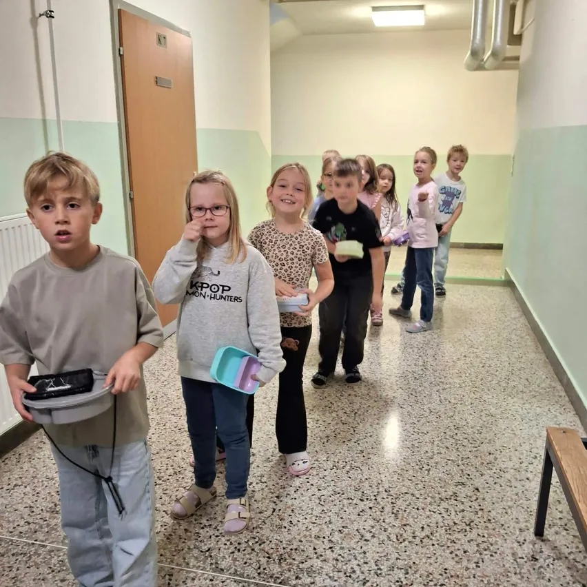 Eine Gruppe von Kindern steht in einem Flur, einige halten Lunchboxen und andere tragen Taschen.