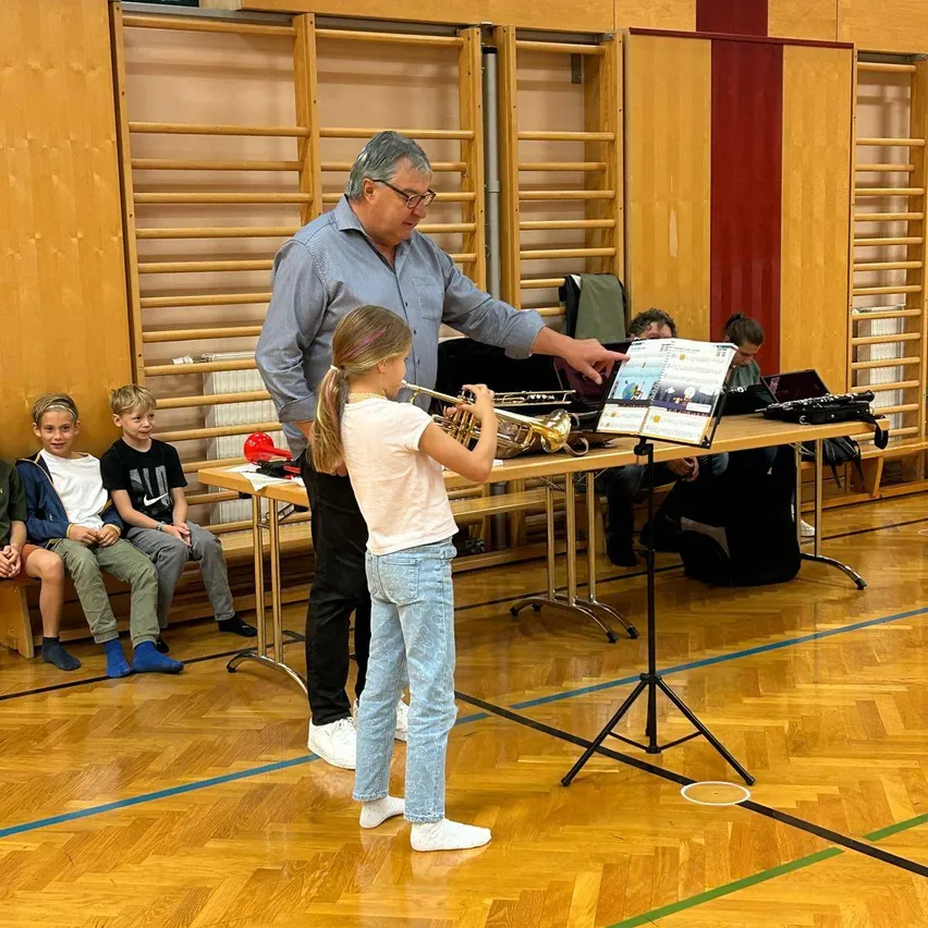 Ein erwachsener Mann unterrichtet ein junges Mädchen, wie man Trompete in einer Turnhalle spielt.