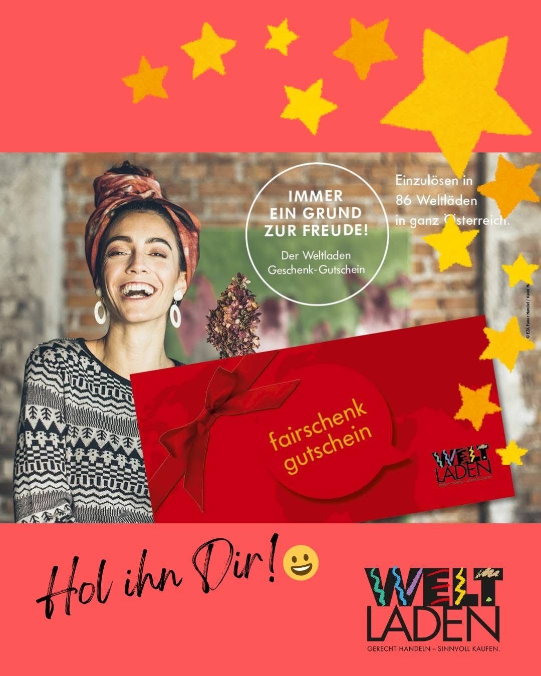 Eine lächelnde Frau hält eine Geschenkkarte mit einem roten Band und einem Strauß Blumen. Auf der Karte steht 'Fairschenk Gutschein'. Der Hintergrund ist eine rote Ziegelsteinwand mit gelben Sternen.
