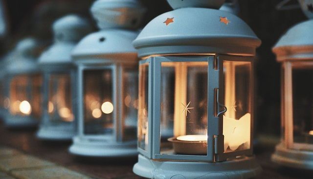 Eine Reihe weißer Laternen mit Sternenmustern ist beleuchtet, eine davon ist angezündet. Die Laterne leuchtet warm und wirft ein sanftes Licht.