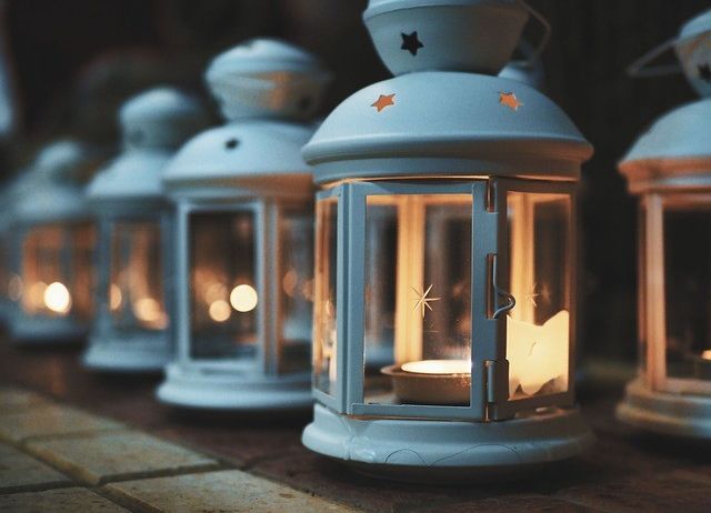 Eine Reihe weißer Laternen mit Sternenmustern ist beleuchtet, eine davon ist angezündet. Die Laterne leuchtet warm und wirft ein sanftes Licht.