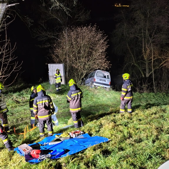 Feuerwehrleute stehen nachts auf einem Hang und bereiten sich darauf vor, einen in einer Rinne steckengebliebenen Lieferwagen zu retten. Sie tragen gelbe Helme und Sicherheitsausrüstung.